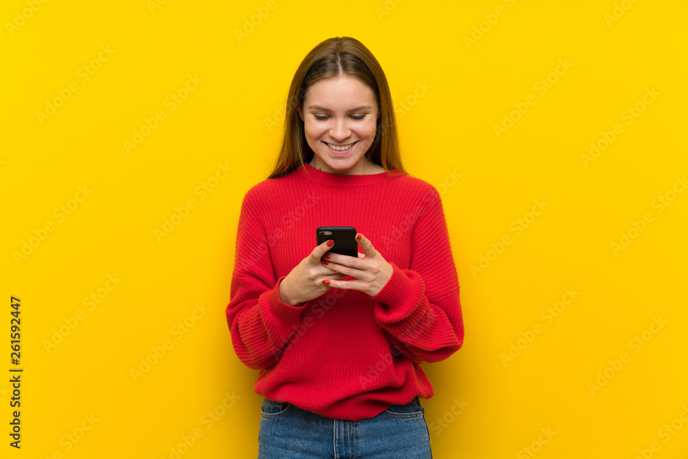 Young woman over yellow wall sending a message with the mobile Young woman over yellow wall sending a message with the mobile