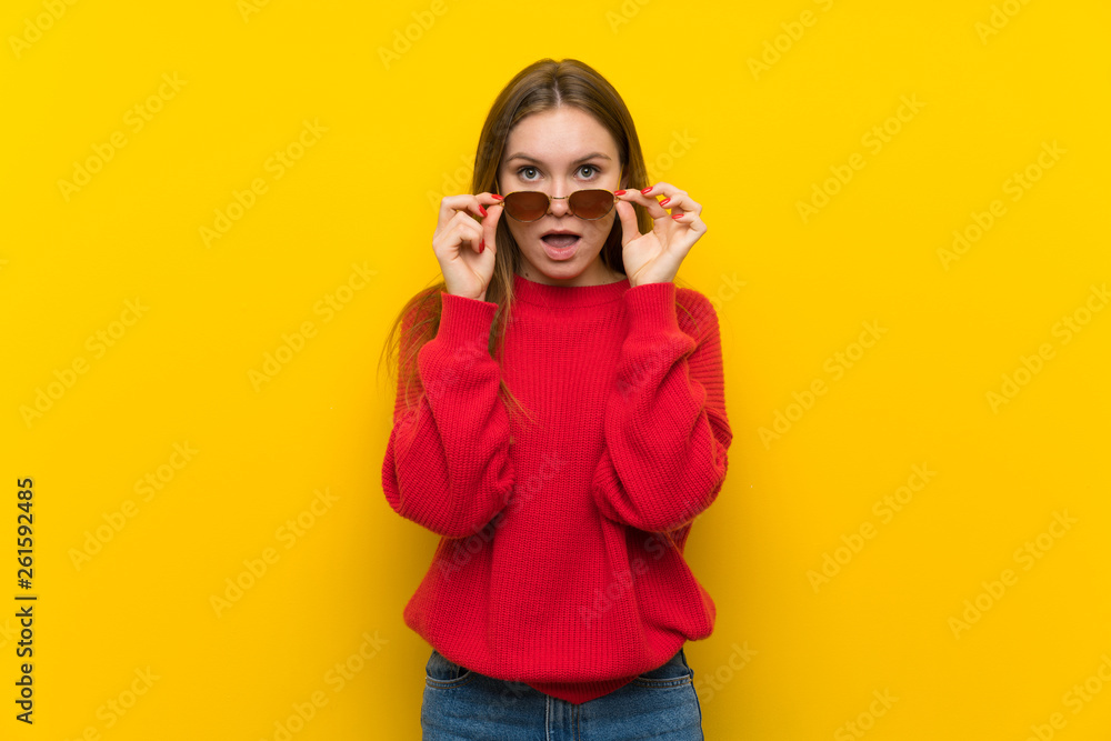 Young woman over yellow wall with glasses and surprised