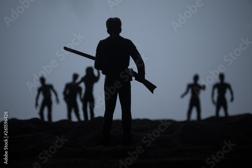 Man with riffle against zombie attack. Zombie apocalypse. Scary view of blurred zombies at cemetery and spooky cloudy sky with fog.
