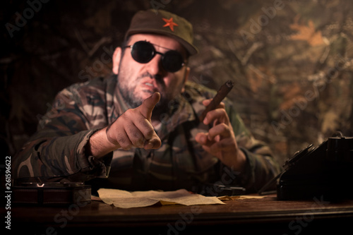 The evil dictator sitting on table. Angry communist general sitting at headquarter or Cuban commander in dark room.