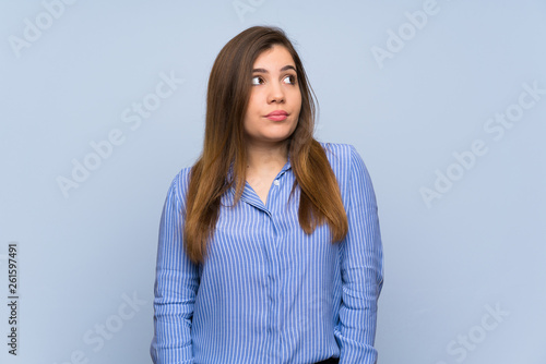 Young girl over isolated blue wall making doubts gesture looking side © luismolinero
