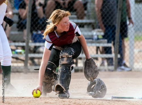 Fotografie Skilled softbaall catcher with red hair and protective gear gaining a grip on the loose ball while looking up field