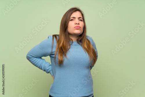Young girl over green wall suffering from backache for having made an effort