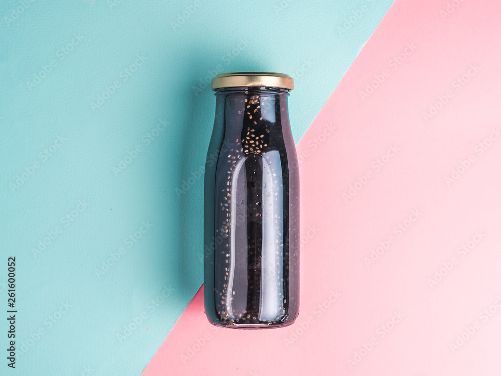 Detox activated charcoal black chia water or mocktail on colorful blue and pink background. Bottle with black chia infused water.Detox drink idea and recipe.Vegan food and drink.Top view