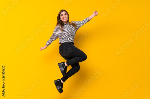 Fototapeta Naklejka Na Ścianę i Meble -  A full-length shot of a Young girl  jumping over isolated yellow background