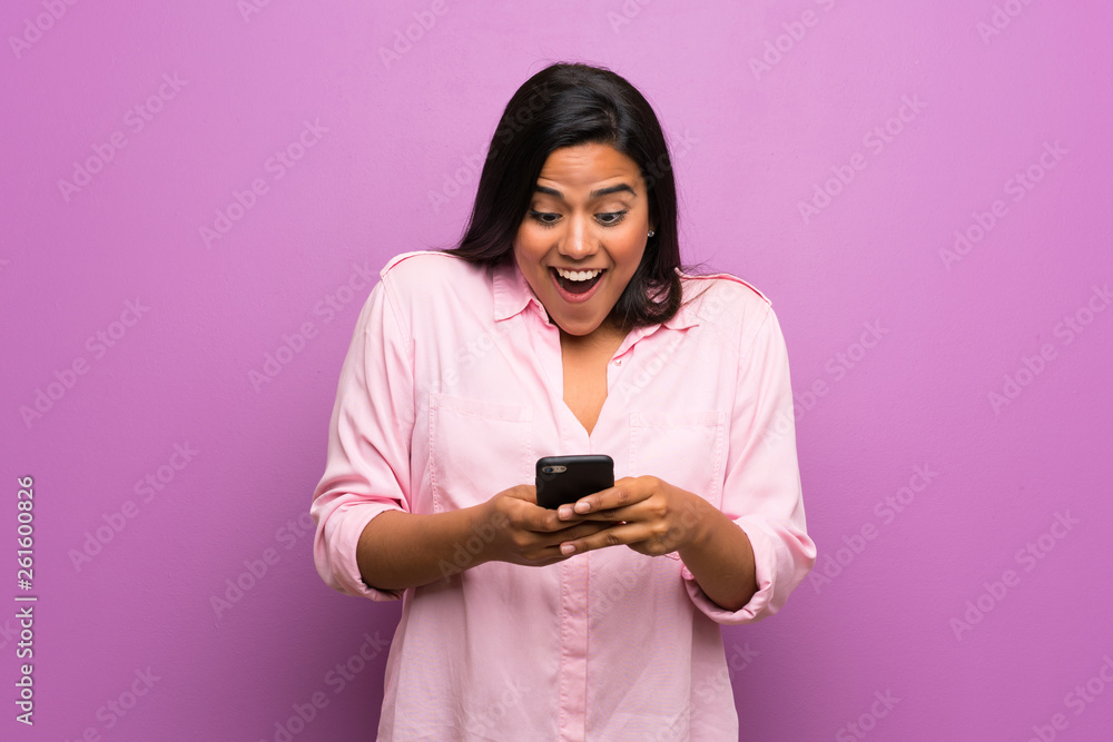 Young Colombian girl over purple wall surprised and sending a message Young Colombian girl over purple wall surprised and sending a message