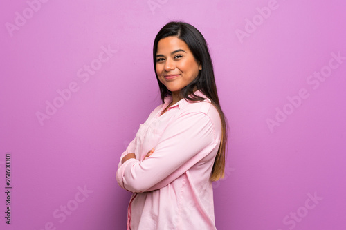 Young Colombian girl over purple wall with arms crossed and looking forward