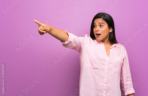 Young Colombian girl over purple wall pointing away