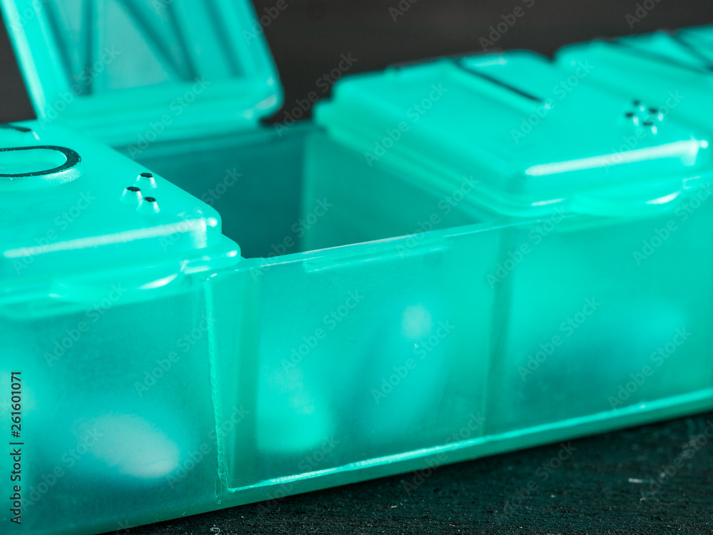 Extreme close up of seven day pill box with pills. Green pill-box with tuesday pills visible. Open pill box on black background Extreme close up of seven day pill box with pills. Green pill-box with tuesday pills visible. Open pill box on black background