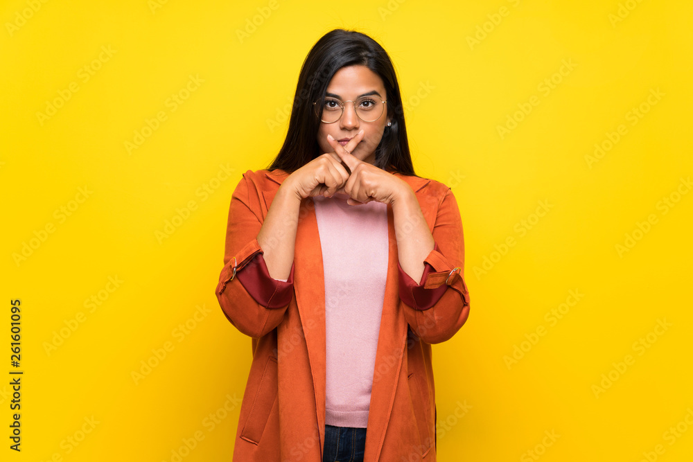 Young Colombian girl over yellow wall showing a sign of silence gesture Young Colombian girl over yellow wall showing a sign of silence gesture