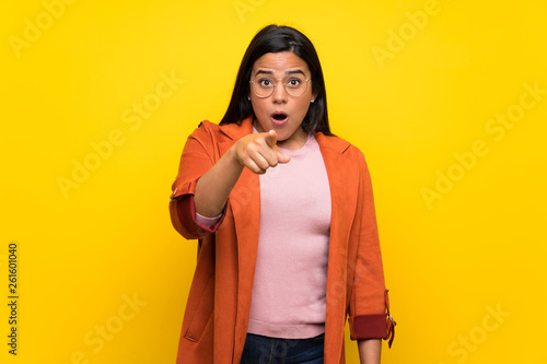 Young Colombian girl over yellow wall surprised and pointing front