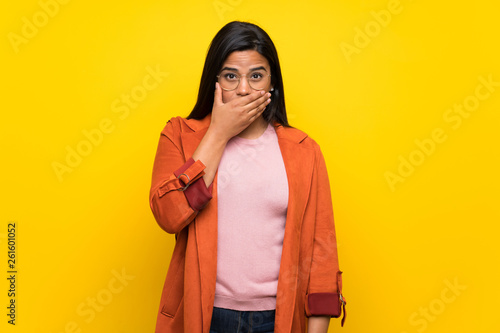 Young Colombian girl over yellow wall covering mouth with hands for saying something inappropriate © luismolinero