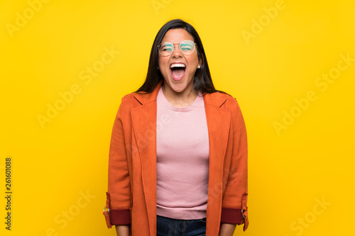 Young Colombian girl over yellow wall shouting to the front with mouth wide open © luismolinero