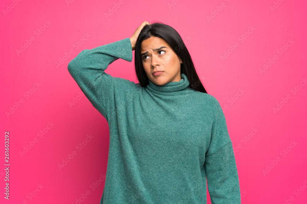 Fototapeta premium Young Colombian girl with green sweater having doubts while scratching head