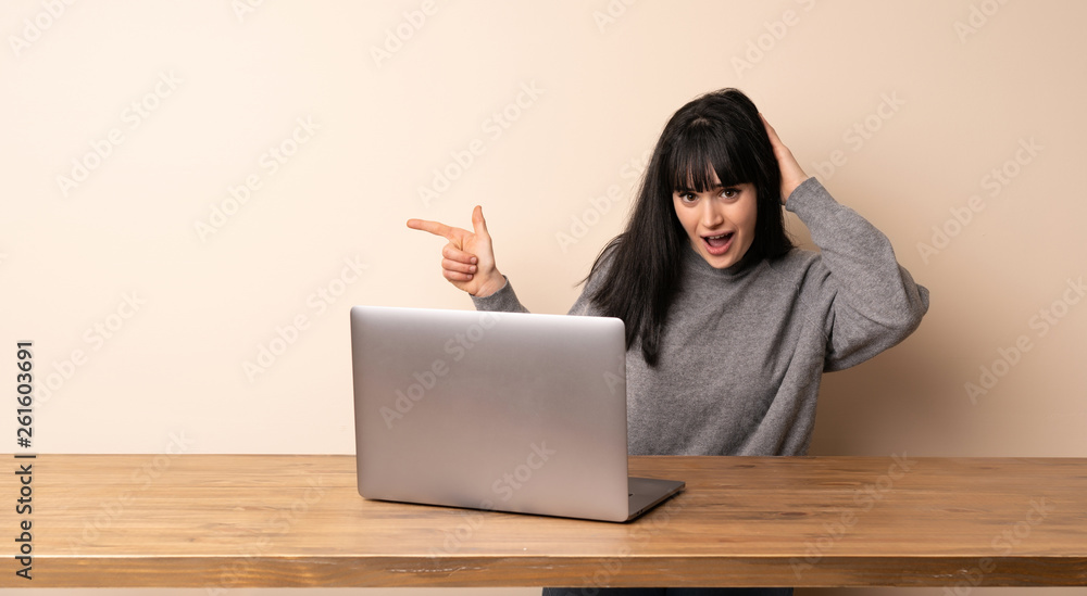 Young woman working with her laptop surprised and pointing finger to the side Young woman working with her laptop surprised and pointing finger to the side