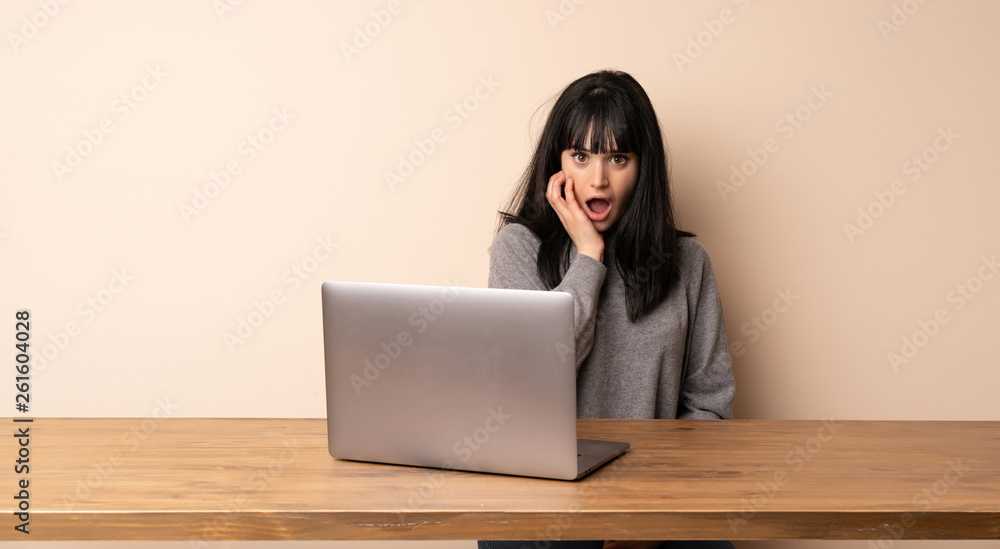 Young woman working with her laptop surprised and shocked while looking right Young woman working with her laptop surprised and shocked while looking right
