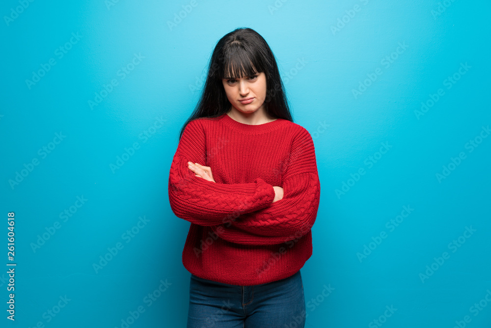 Woman with red sweater over blue wall feeling upset Woman with red sweater over blue wall feeling upset