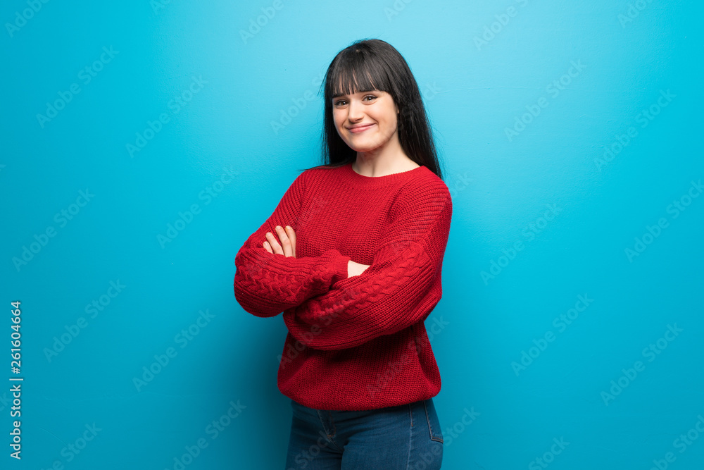 Woman with red sweater over blue wall with arms crossed and looking forward Woman with red sweater over blue wall with arms crossed and looking forward