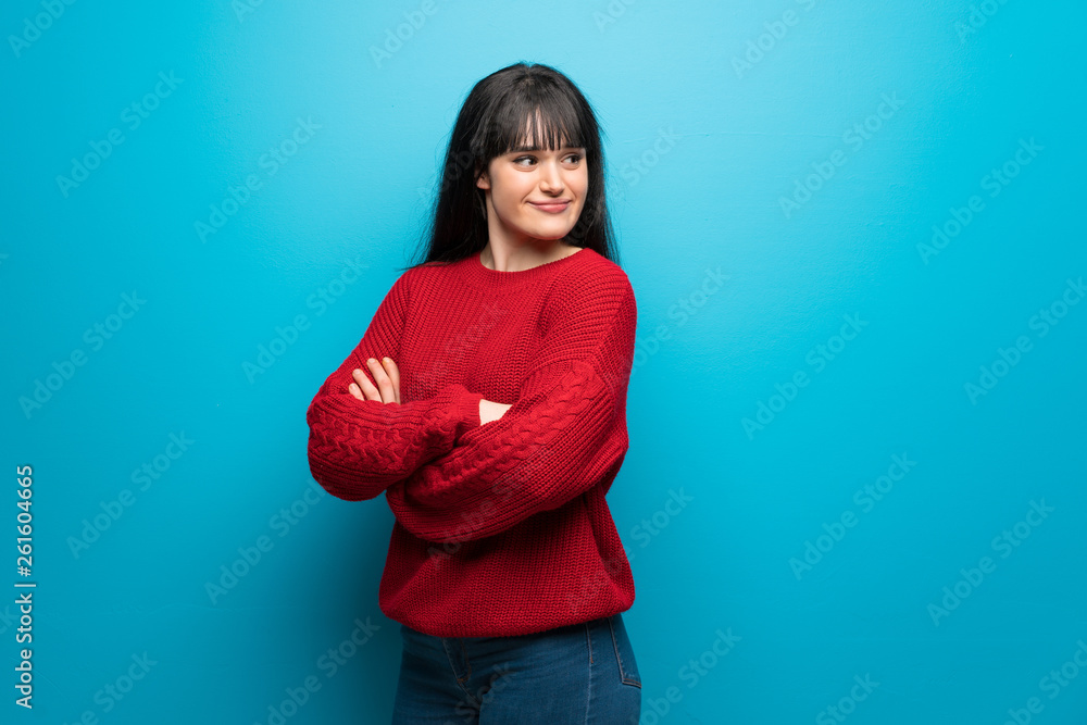 Woman with red sweater over blue wall with arms crossed and happy Woman with red sweater over blue wall with arms crossed and happy