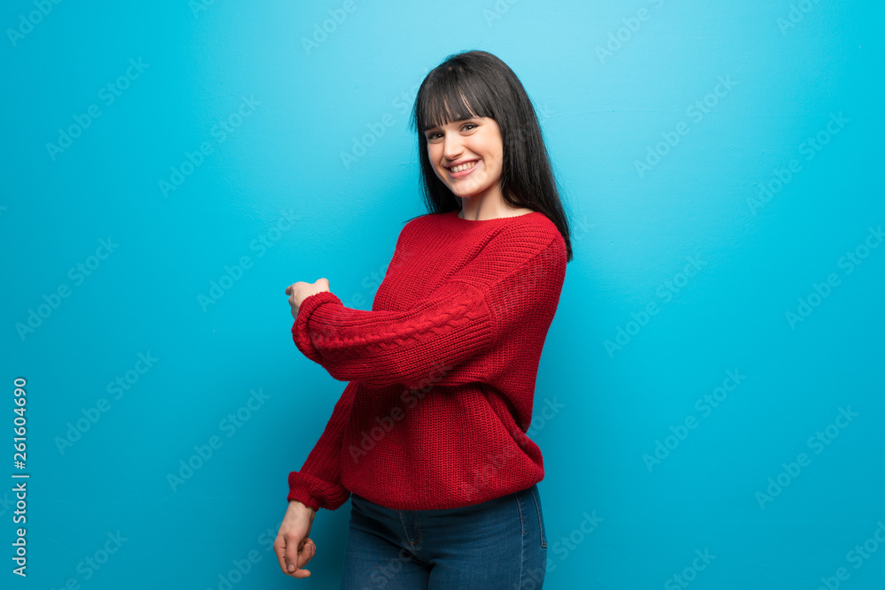Woman with red sweater over blue wall pointing back Woman with red sweater over blue wall pointing back