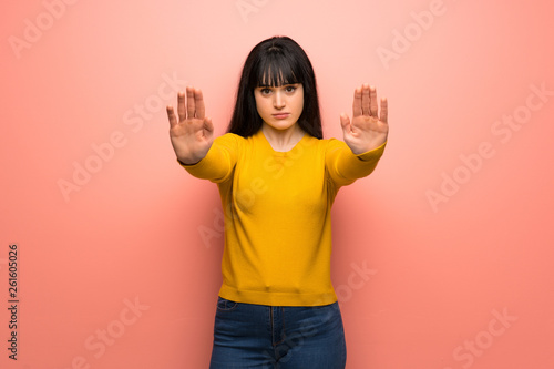 Woman with yellow sweater over pink wall making stop gesture and disappointed