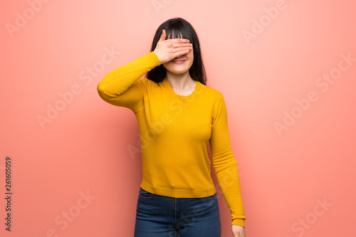Woman with yellow sweater over pink wall covering eyes by hands. Do not want to see something