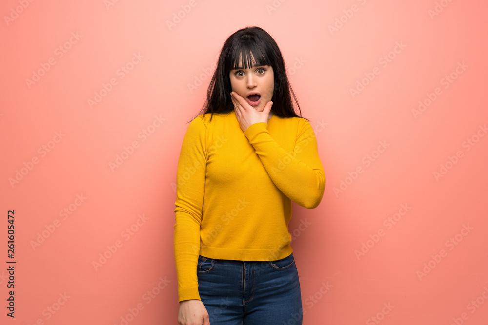 Woman with yellow sweater over pink wall surprised and shocked while looking right Woman with yellow sweater over pink wall surprised and shocked while looking right
