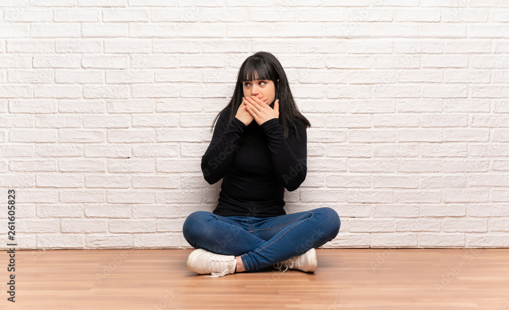 Woman sitting on the floor covering mouth and looking to the side Woman sitting on the floor covering mouth and looking to the side