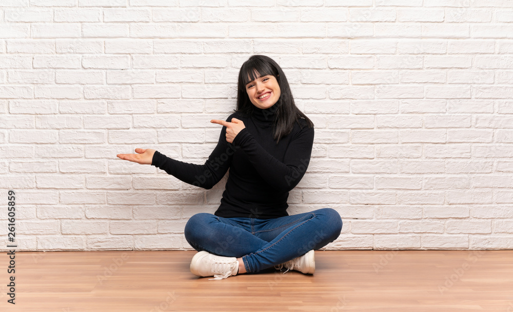 Woman sitting on the floor holding copyspace imaginary on the palm to insert an ad Woman sitting on the floor holding copyspace imaginary on the palm to insert an ad