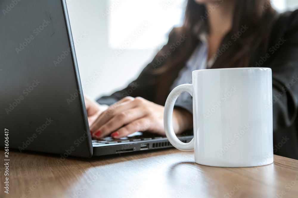 white cup on a desk with a laptop in the background and some female hands white cup on a desk with a laptop in the background and some female hands