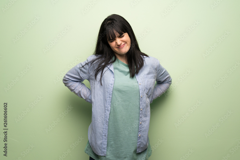 Young woman over green wall suffering from backache for having made an effort Young woman over green wall suffering from backache for having made an effort