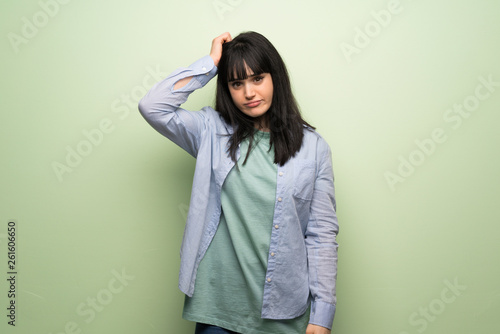 Young woman over green wall with an expression of frustration and not understanding