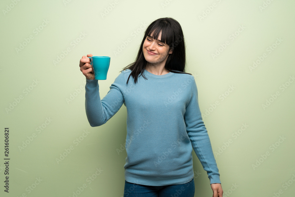 Young woman over green wall holding a hot cup of coffee Young woman over green wall holding a hot cup of coffee