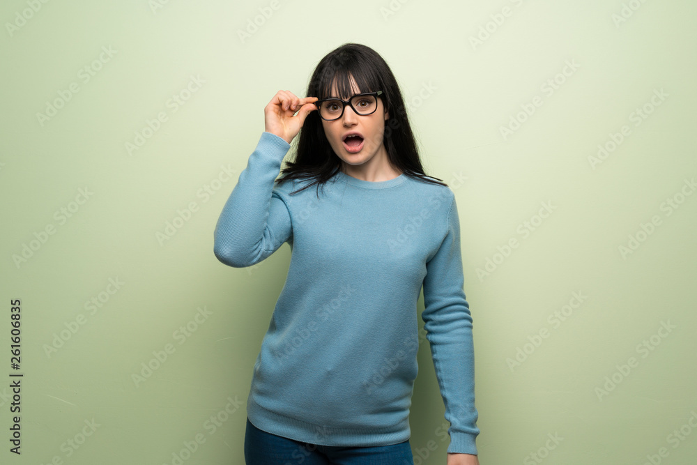 Young woman over green wall with glasses and surprised Young woman over green wall with glasses and surprised