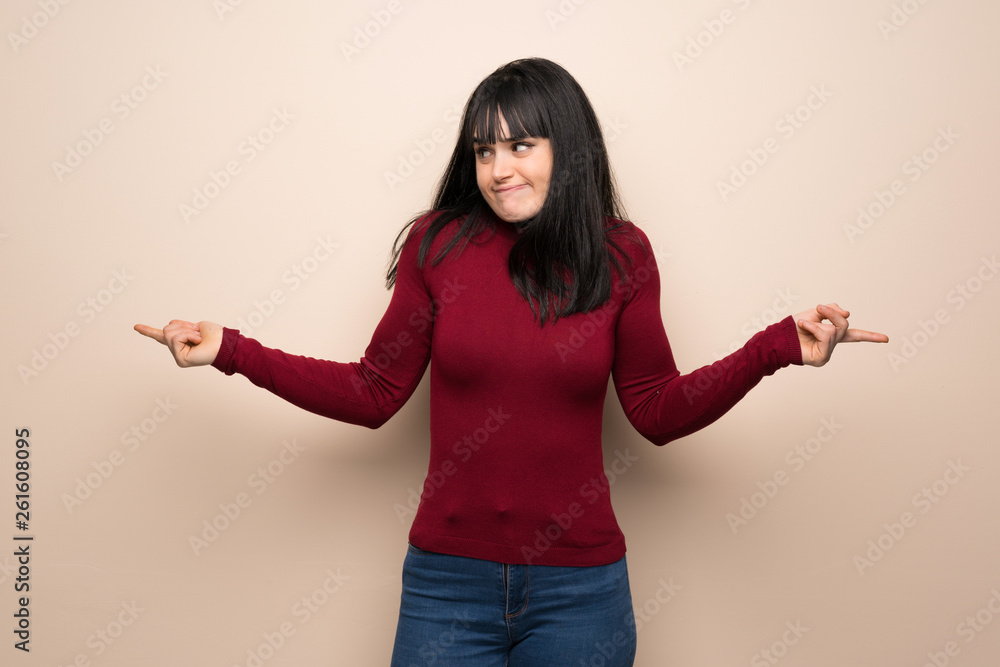 Young woman with red turtleneck pointing to the laterals having doubts Young woman with red turtleneck pointing to the laterals having doubts