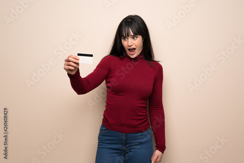 Young woman with red turtleneck holding a credit card and surprised