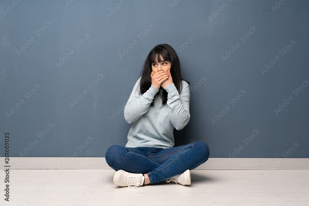 Woman sitting on the floor covering mouth and looking to the side Woman sitting on the floor covering mouth and looking to the side