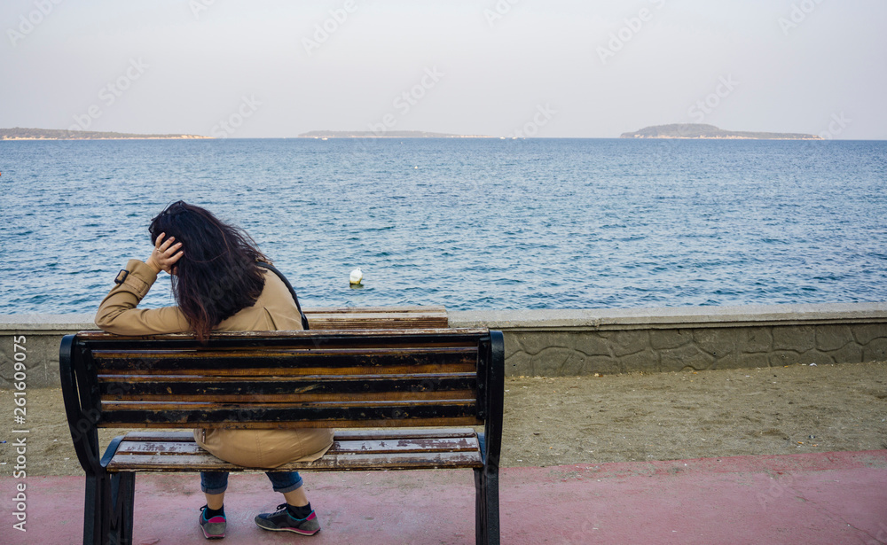 Young sad depressed woman sit alone on bench, looking at distant sea / seascape horizon. Time to go, say goodbye. Miss someone. Desire, hope to go far away. Unhappy girl feel lonely at seaside outdoor