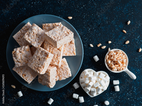 Homemade square bars of Marshmallow and crispy rice and ingredients on dark blue background. American dessert with marshmallow and crispy rice. Top view. Copy space photo