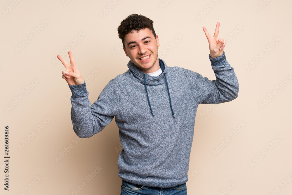 Young man over isolated wall showing victory sign with both hands Young man over isolated wall showing victory sign with both hands