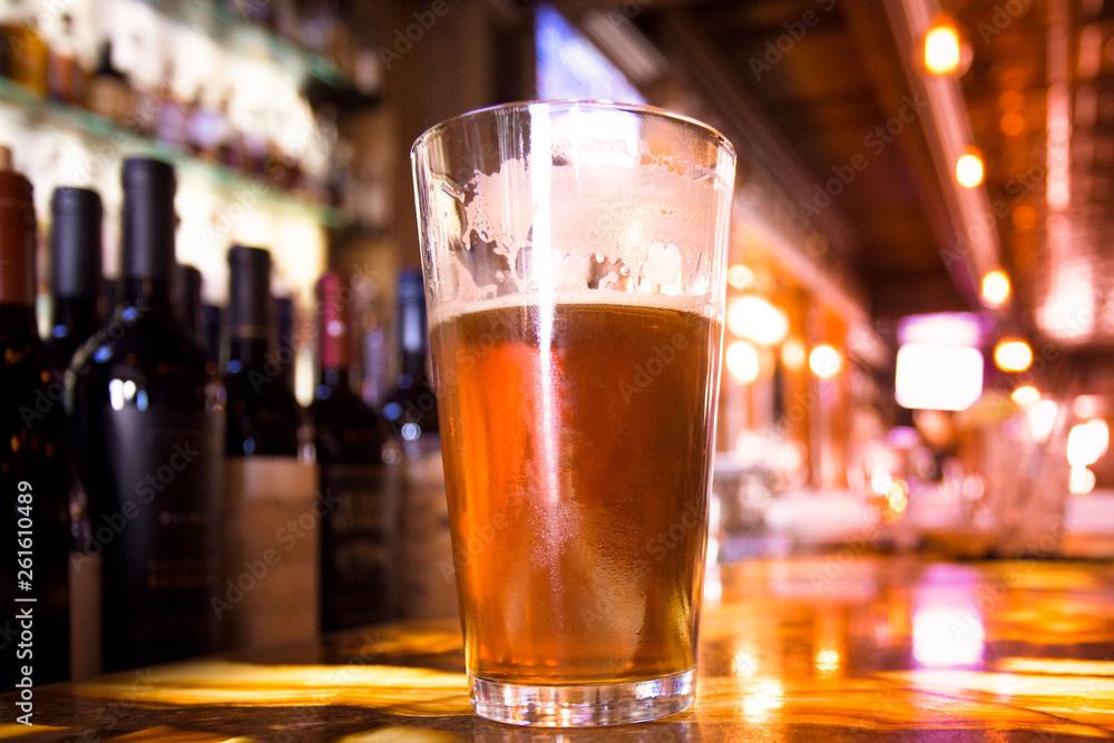 Glass Pint of amber beer with colorful blur of bar in background
