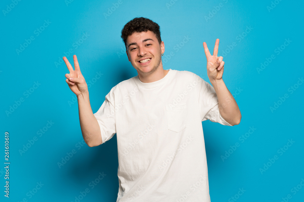 Young man over blue background smiling and showing victory sign with both hands Young man over blue background smiling and showing victory sign with both hands