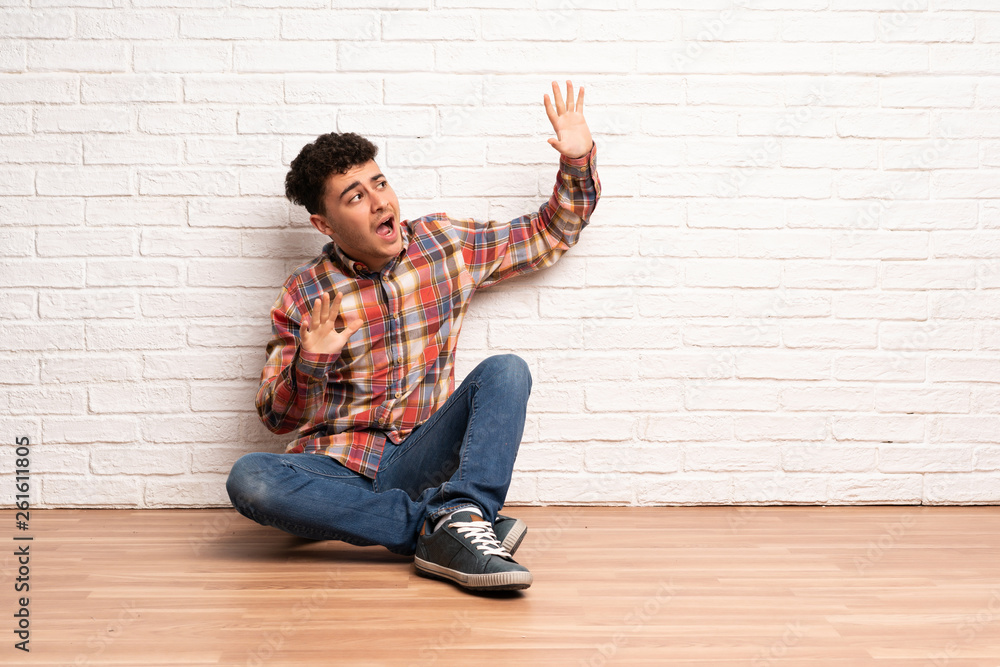 Young man sitting on the floor nervous and scared Young man sitting on the floor nervous and scared