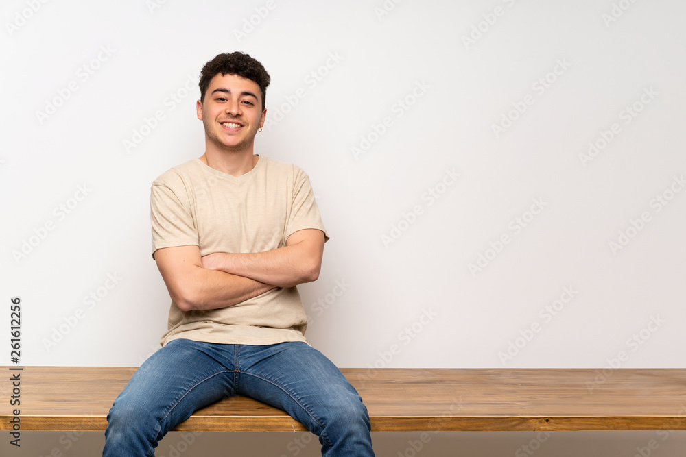 Young man sitting on table keeping the arms crossed in frontal position Young man sitting on table keeping the arms crossed in frontal position