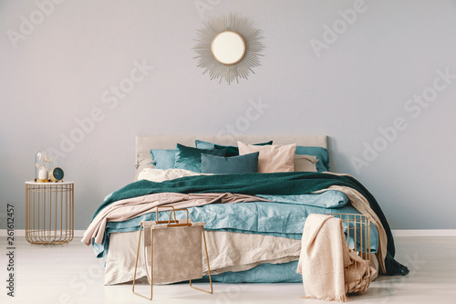 Sun shape like golden mirror on the empty wall of classy bedroom interior with king size bed