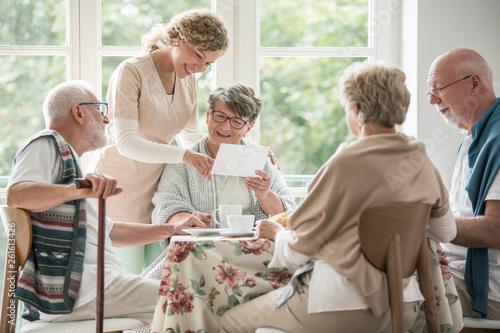 Group of seniors drinking tea together. Nurse is showing a photo to her female patient photo