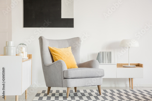 Yellow pillow on grey armchair in fashionable living room interior with black and white painting photo