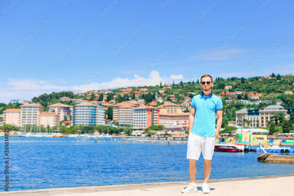 Young man in stylish clothes and sunglasses standing on pier on