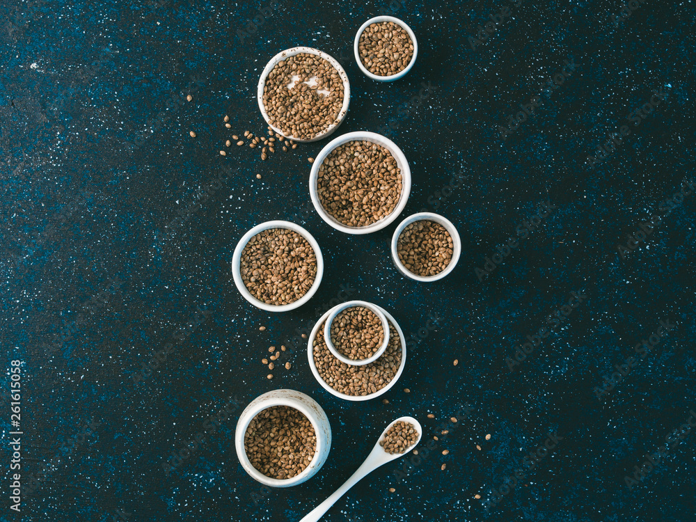 Hemp seeds in small white bowls and spoon on dark blue tabletop. Set of small bowls with raw organic unrefined hemp seed. Superfood and vegan concept. Top view or flat lay.Copy space for text. Hemp seeds in small white bowls and spoon on dark blue tabletop. Set of small bowls with raw organic unrefined hemp seed. Superfood and vegan concept. Top view or flat lay.Copy space for text.
