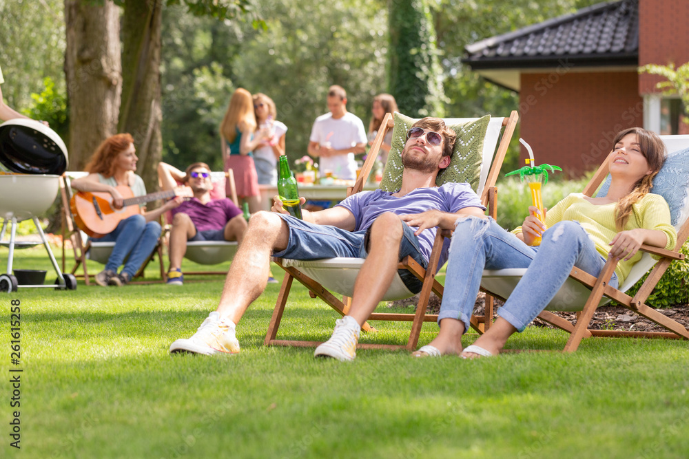 Smiling woman and man relaxing on sunbeds during grill party in the garden Smiling woman and man relaxing on sunbeds during grill party in the garden